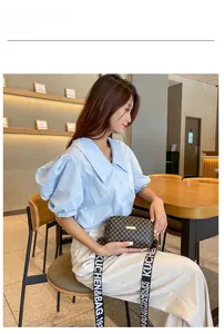 Détail d'un sac caméra marron monogrammé avec large bandoulière logo dans un café
