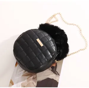 Détail du sac bandoulière rond matelassé avec plaque dorée et pompon en fausse fourrure