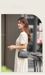 Détail d'un sac bandoulière matelassé noir avec chaîne dorée et robe fleurie