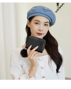 Close-up of woven leather mini wallet with gold zipper and decorative black pompom detail