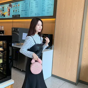 Sac à main rond rose matelassé avec poignée en fourrure et plaque dorée porté par un mannequin