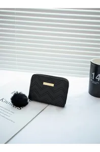 Détail du petit porte-monnaie matelassé noir avec plaque dorée et pompon en fourrure