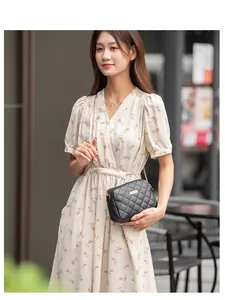 Sac bandoulière noir matelassé avec chaîne dorée porté sur une robe à fleurs