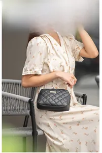 Détail d'un sac bandoulière noir matelassé avec plaque dorée et bandoulière en chaîne