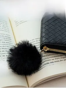 Close-up of black woven leather wallet with gold zipper and a soft plush pom-pom charm