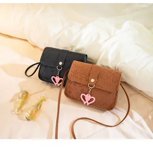 Detail of embossed crossbody bags with heart charms in black and brown colors