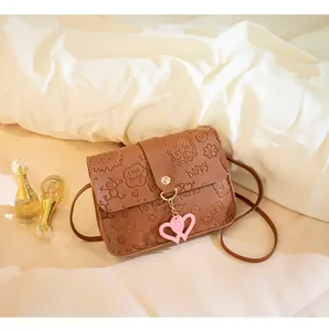 Close-up of brown crossbody bag featuring detailed cartoon embossing and a heart charm