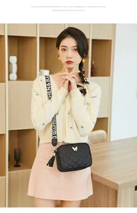 Détail du sac bandoulière noir matelassé avec breloque papillon dorée et pompon