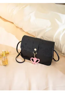 Detailed view of the embossed leather texture and pink heart charms on a black crossbody bag