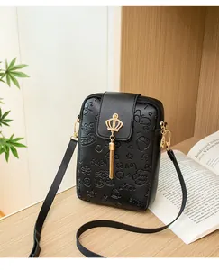 Detail of black pebbled leather phone bag with gold crown buckle and long tassel charm