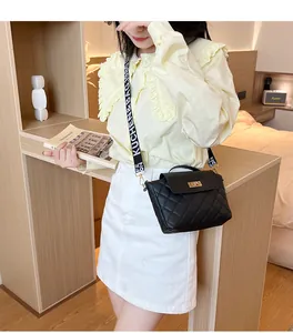 Close-up of black quilted crossbody bag with wide logo strap and gold metallic lock detail