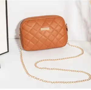 Détail d'un sac bandoulière marron matelassé avec plaque métallique dorée et bandoulière chaîne