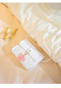 Detailed view of white crossbody bag with embossed graffiti and heart-shaped charm