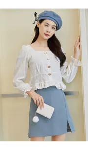 Close-up of white long sleeve top with textured fabric, square neck and gold buttons