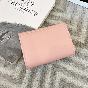 Mini porte-monnaie rose pâle en cuir avec surpiqûres sur un livre décoratif chic