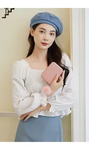 Close-up of a pink woven texture wallet with a fluffy pom-pom charm held by a model