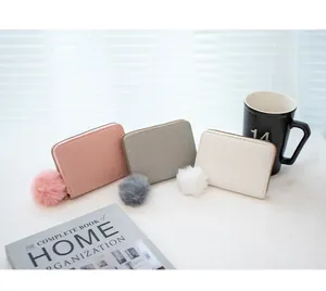Detail of woven texture short zip wallets in pink, grey and white with fur pompom charms