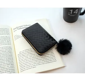 Close-up of black woven leather coin purse with golden zipper and plush ball keychain