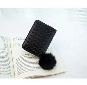 Close-up of black woven leather coin purse with a soft pom-pom keychain on a book