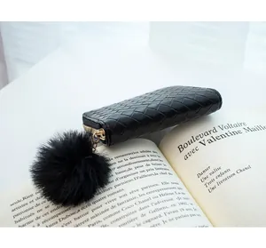 Detail of woven black leather wallet with golden zipper and plush pom-pom keychain