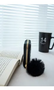 Close-up of black woven coin purse with gold zipper and decorative plush pom-pom charm