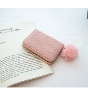 Detailed close-up of pink woven leather coin purse with fuzzy pompom on a book