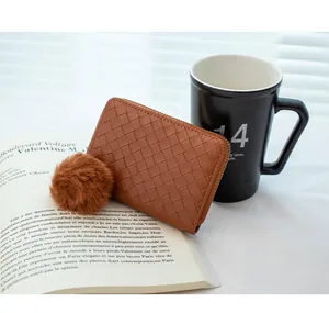 Detail of woven brown leather coin purse with zipper and pom-pom charm on an open book