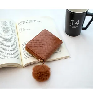 Brown woven texture small zip wallet featuring a decorative plush pompom on a book
