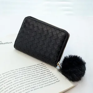 Black woven leather small zipper wallet with plush pom-pom charm on a book background