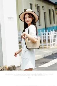 Detail of beige straw tote bag with black leather handles and matching summer straw hat