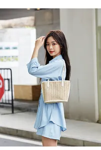 Detailed view of woven tote bag with white leather straps styled on a blue shirt dress