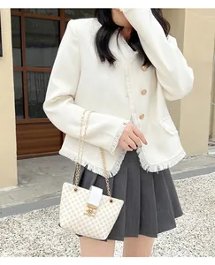 Detail of white tweed jacket with gold buttons paired with a mini patterned chain bucket bag