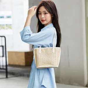 Beige woven straw tote bag with white leather handles carried by a model outdoors