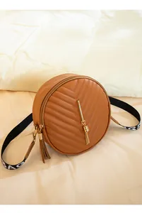 Detailed close-up of a caramel round crossbody bag with V-quilt pattern and gold tassel