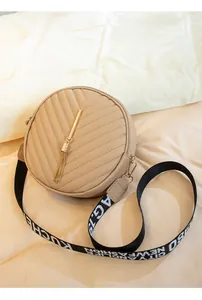 Detail of round beige crossbody bag with V-quilt pattern and golden fringe tassel