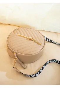 Macro view of beige quilted round crossbody bag with gold tassel and lettered strap