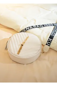 Detail of white quilted round crossbody bag with gold tassel and lettered strap