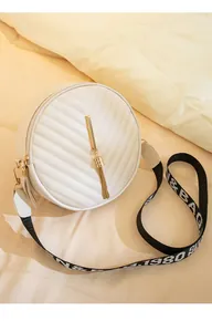 Detail of white quilted round crossbody bag with gold tassel and wide patterned strap