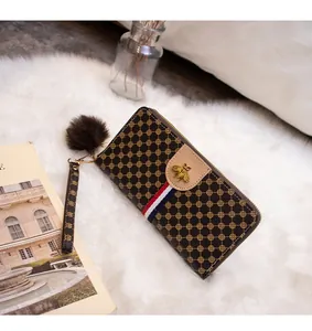 Detail of long brown wallet with bee logo, striped ribbon and faux fur pompom charm