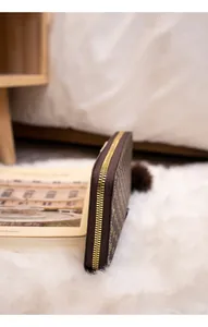 Detail of a brown monogram long wallet with gold zipper standing on white faux fur rug