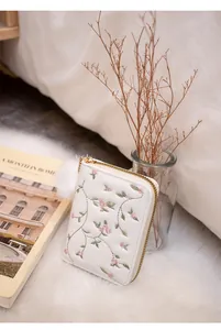 Detailed embroidery of pink flowers and soft pom-pom charm on a cream mini wallet
