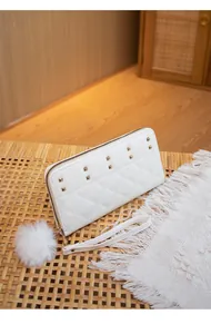 Detail of white quilted wallet with gold studs, wrist strap and plush ball ornament