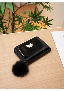 Detail of black patent leather wallet featuring butterfly ornament and fluffy pompom charm