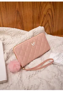 Detail of pink quilted wallet with butterfly metal ornament and fluffy pompom keychain