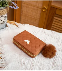 Close-up of quilted brown mini purse with white butterfly charm and plush pompom accessory