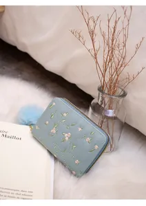 Detailed close-up of light blue wallet with floral embroidery and soft pompom pendant
