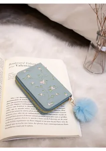 Detail of floral embroidery on light blue faux leather wallet with faux fur pompom