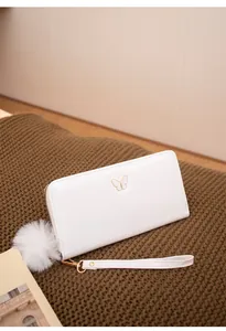 Détail du portefeuille en cuir blanc avec décor papillon doré et pompon doux attaché