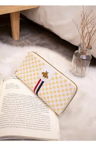 Detail of white wallet with yellow circles, bee ornament, and red-blue stripe on a book