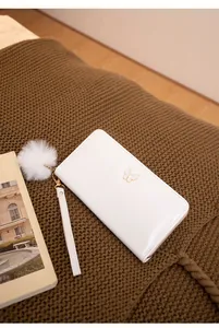 Vue détaillée d'un portefeuille blanc brillant avec logo papillon doré et pompon en fourrure